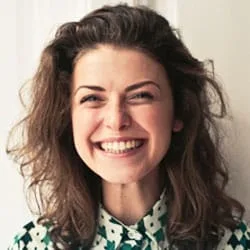 Cuidado Sênior – Mulher jovem sorridente, de cabelos cacheados e blusa estampada, representando uma familiar satisfeita com o cuidado oferecido a um ente querido idoso.