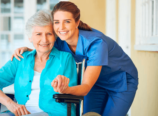 Cuidado Sênior – Cuidadora Residencial sorridente apoia idosa em cadeira de rodas, transmitindo afeto e confiança em ambiente iluminado.