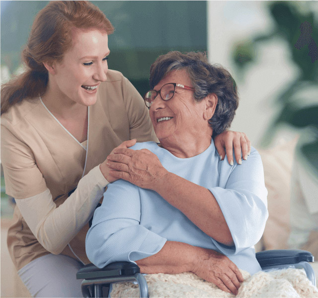 Cuidado Sênior - Cuidadora sorri para idosa em cadeira de rodas, ambas trocando um olhar carinhoso em ambiente acolhedor.