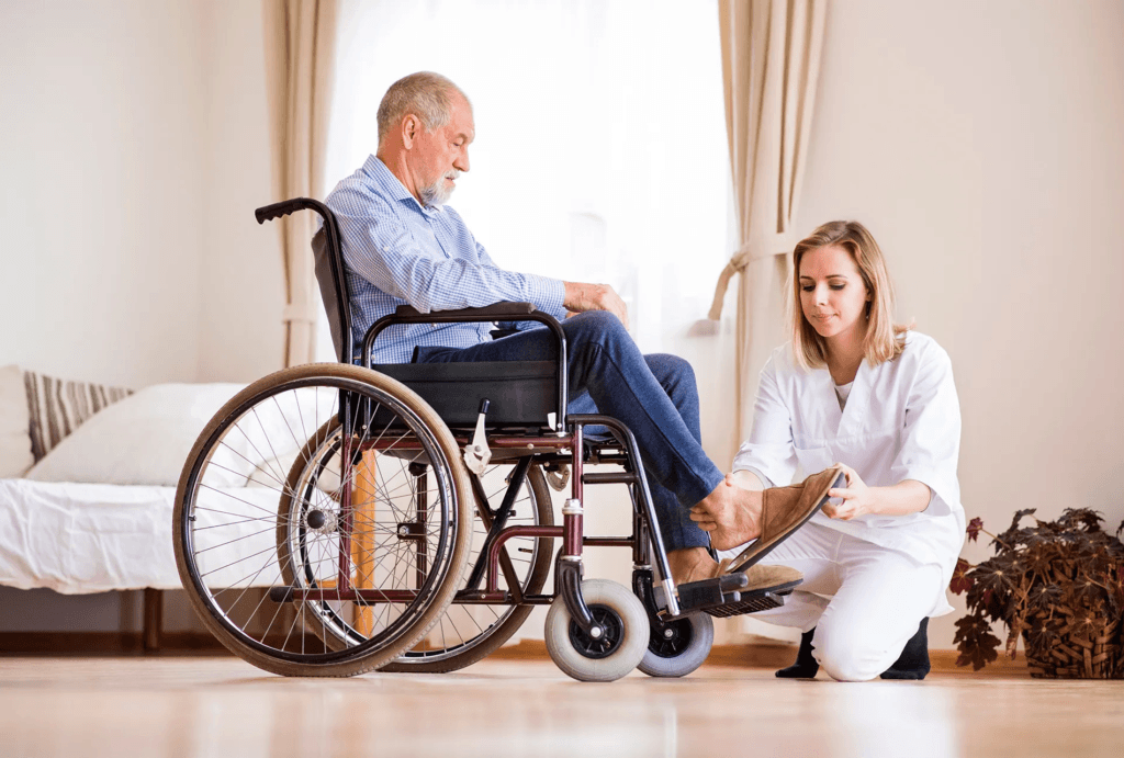 Cuidado Sênior - Cuidadora ajuda idoso em cadeira de rodas a calçar sapato, em ambiente residencial claro e acolhedor.