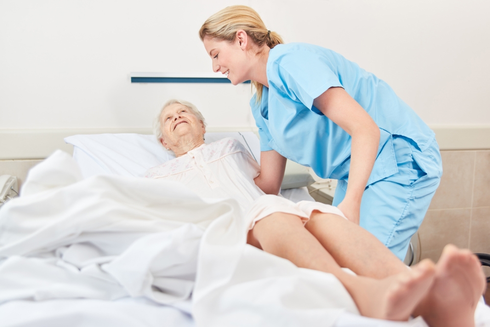 Cuidado Sênior - Cuidadora hospitalar auxilia idosa acamada com cuidado e sorriso, em ambiente hospitalar limpo e acolhedor.