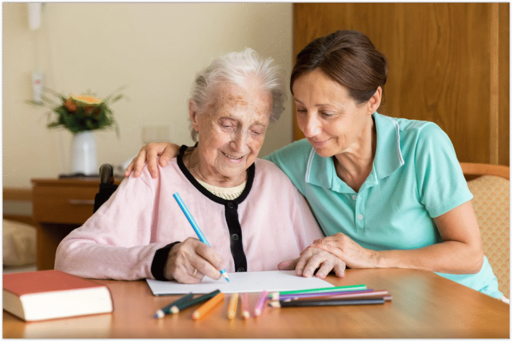 Cuidadora acompanhando idosa com Alzheimer em atividade de desenho para estimulação cognitiva